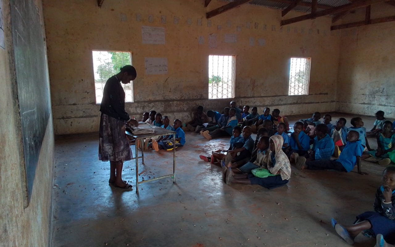 A teacher preparing lesson materials for learners seated inside a classroom