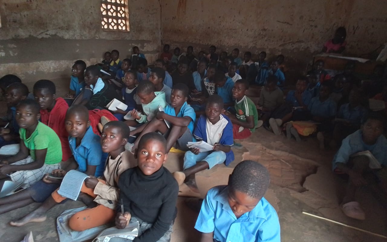 Younger Chipata Primary School learners seated on the classroom floor with exercise books